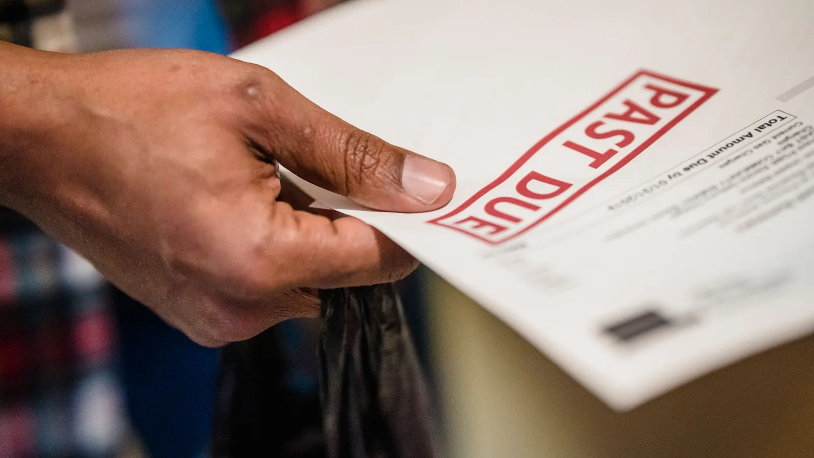 Close-up of a hand holding a white bill stamped PAST DUE in red letters