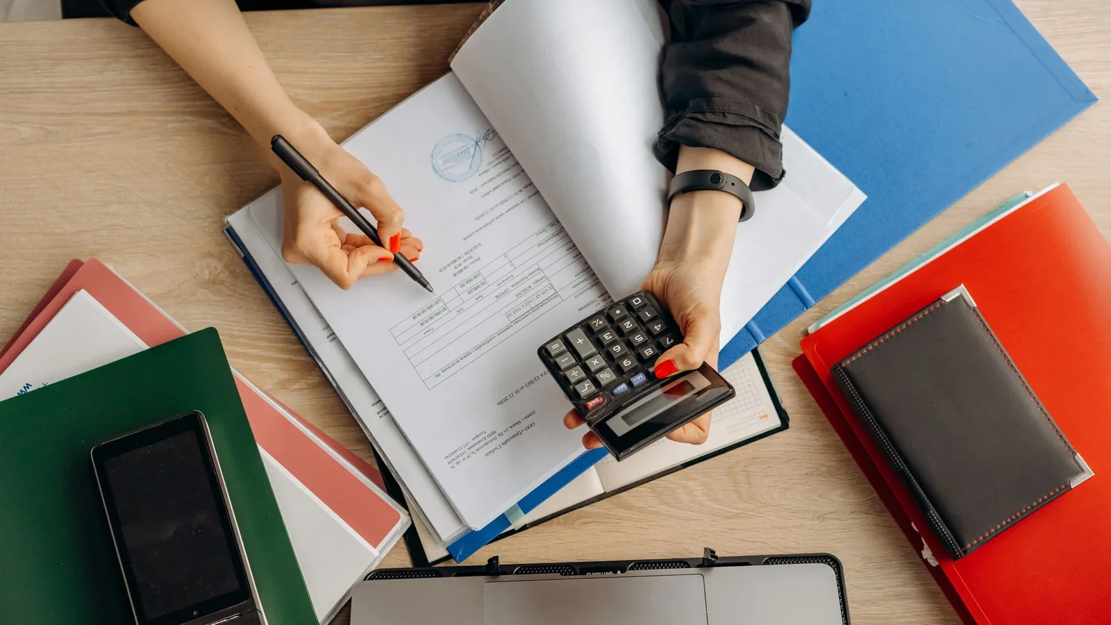Manos revisando documentos financieros con una calculadora en un escritorio