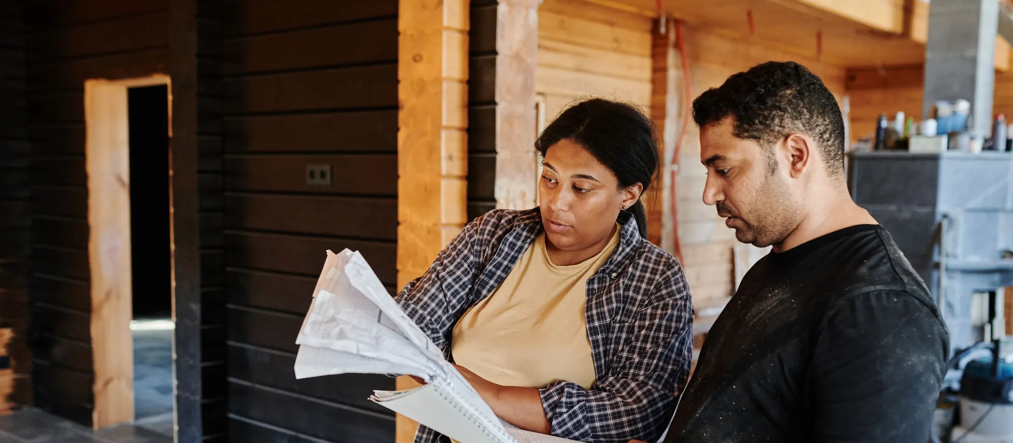 Two contractors reviewing construction plans inside a timber-framed building under construction