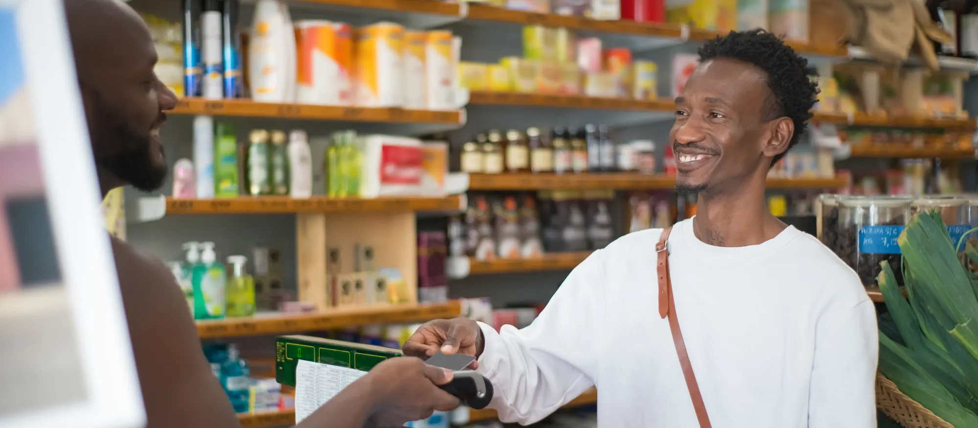 Smiling customer paying by card at the register while the clerk holds the card reader in a neighborhood store