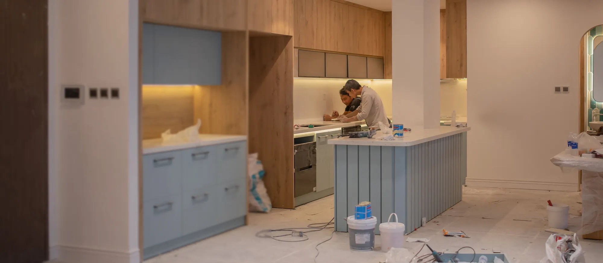 Two installers working at a new kitchen island among cabinets and buckets during a remodel