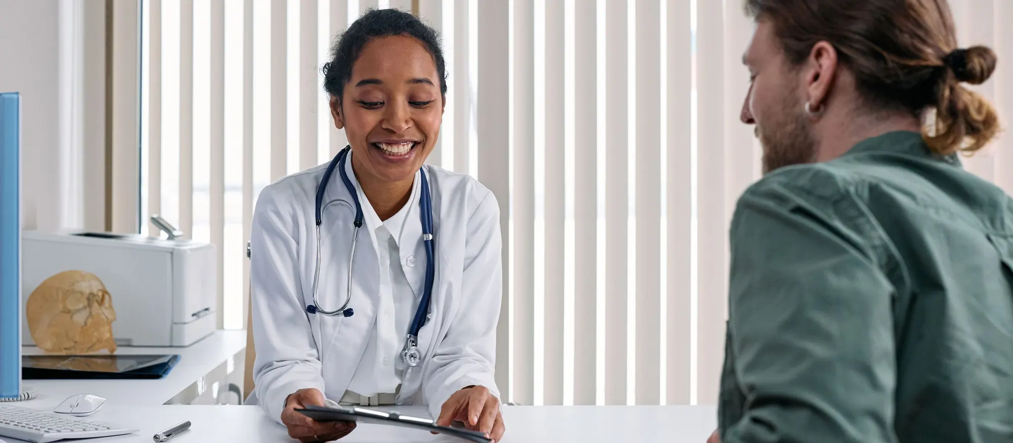 Smiling doctor reviewing results on a tablet with a patient across her office desk