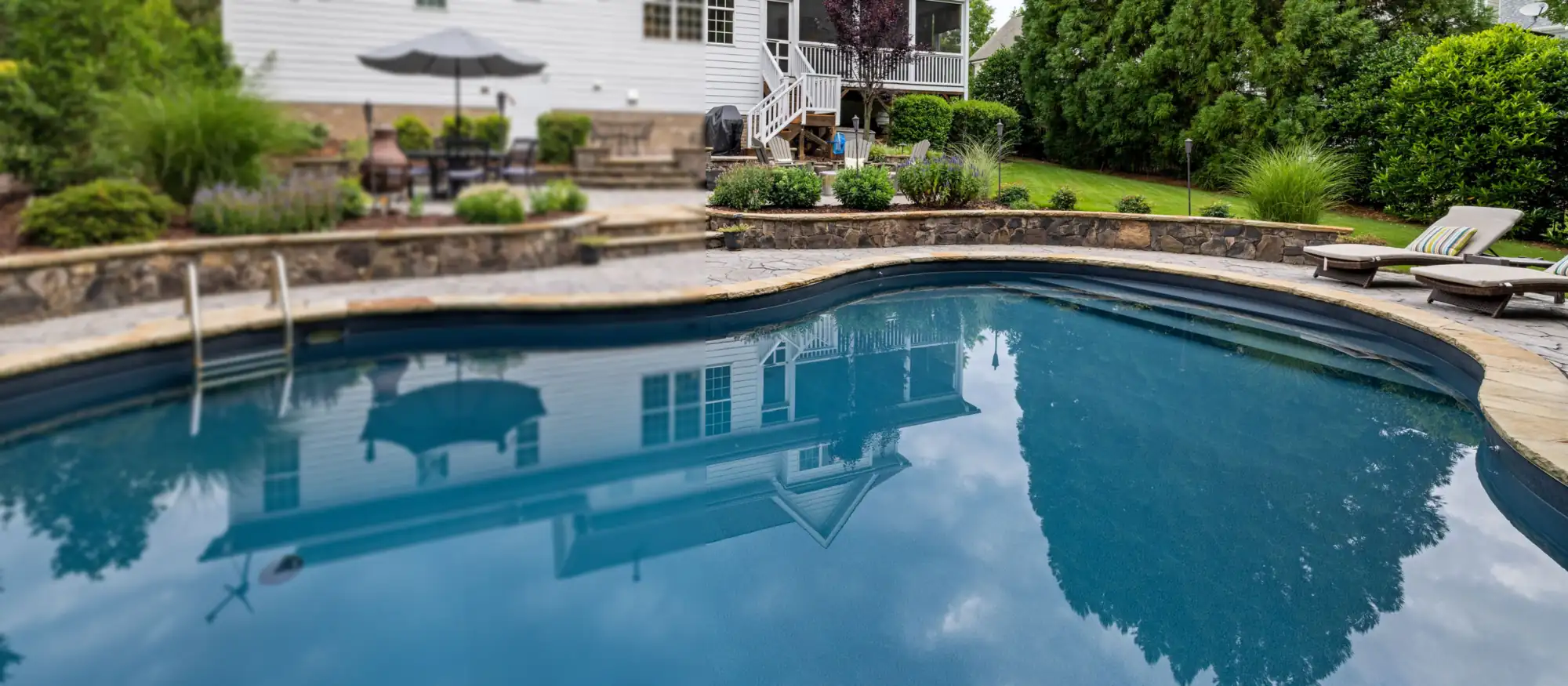 Finished backyard swimming pool with a stone deck and landscaped yard behind a house