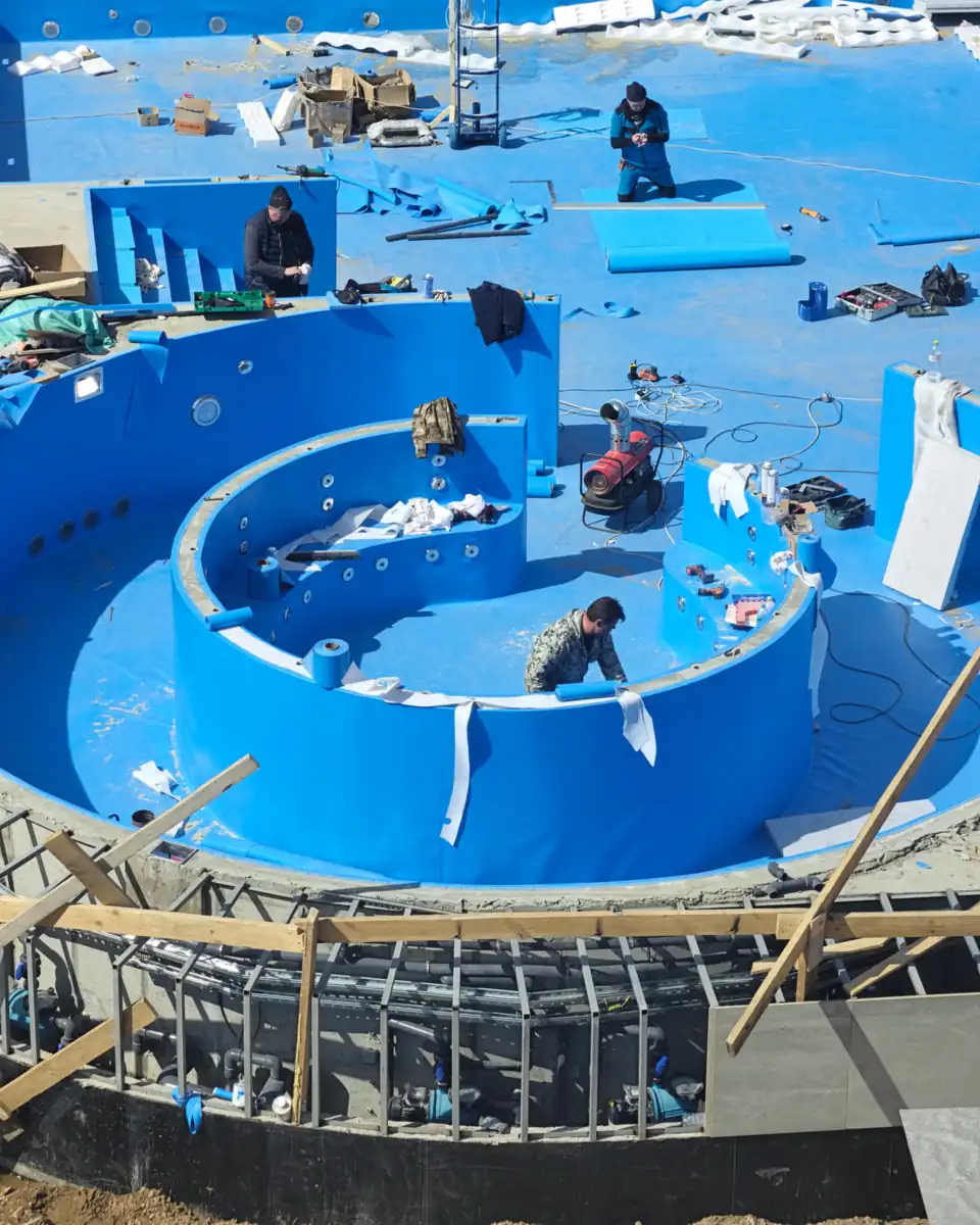 Overhead view of workers finishing the blue shell of a new swimming pool under construction