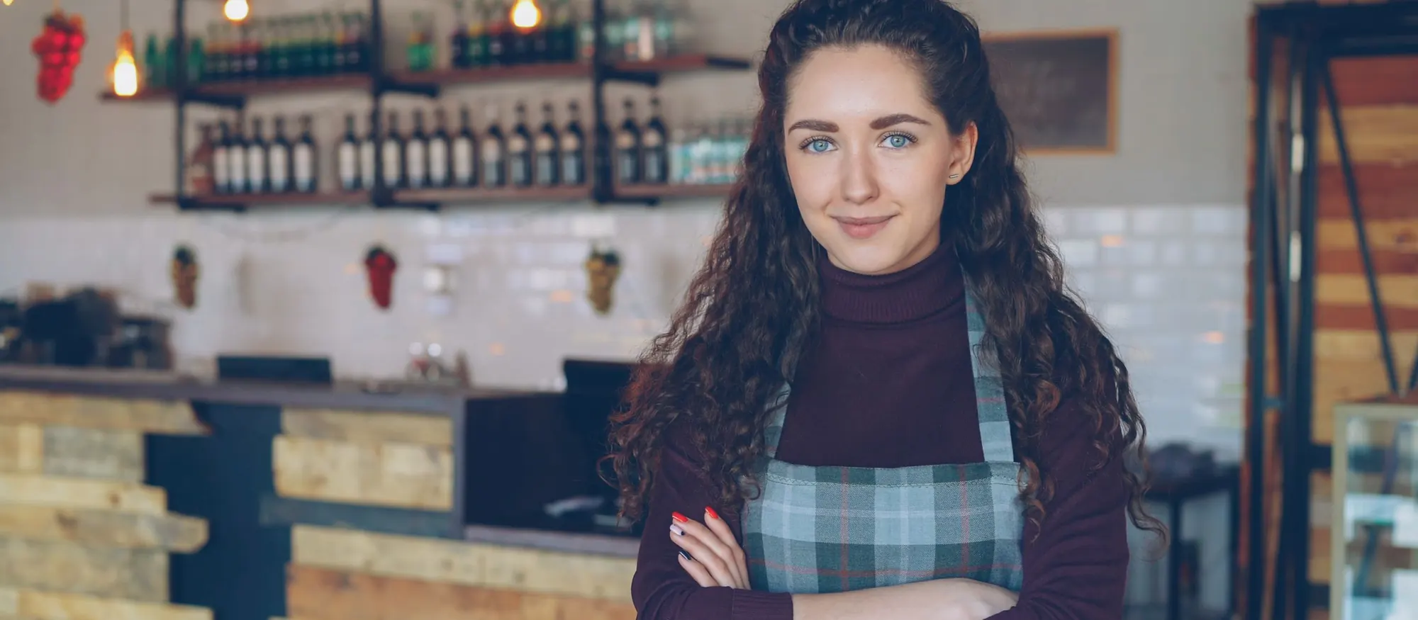 Restaurant owner in a plaid apron standing with arms crossed in front of her counter