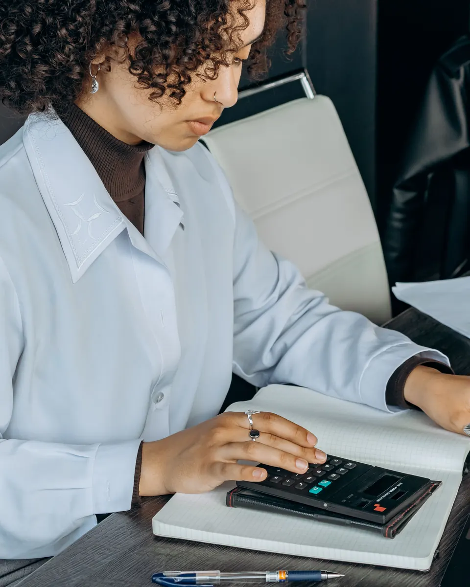 Tax preparer in a light blue blouse working a calculator over an open notebook at her desk