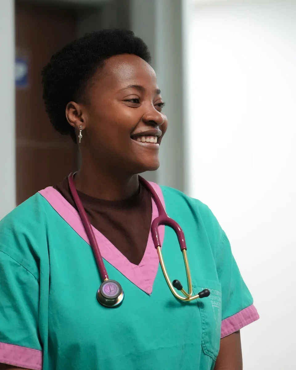 Smiling nurse in teal scrubs with a stethoscope around her neck in a hospital hallway