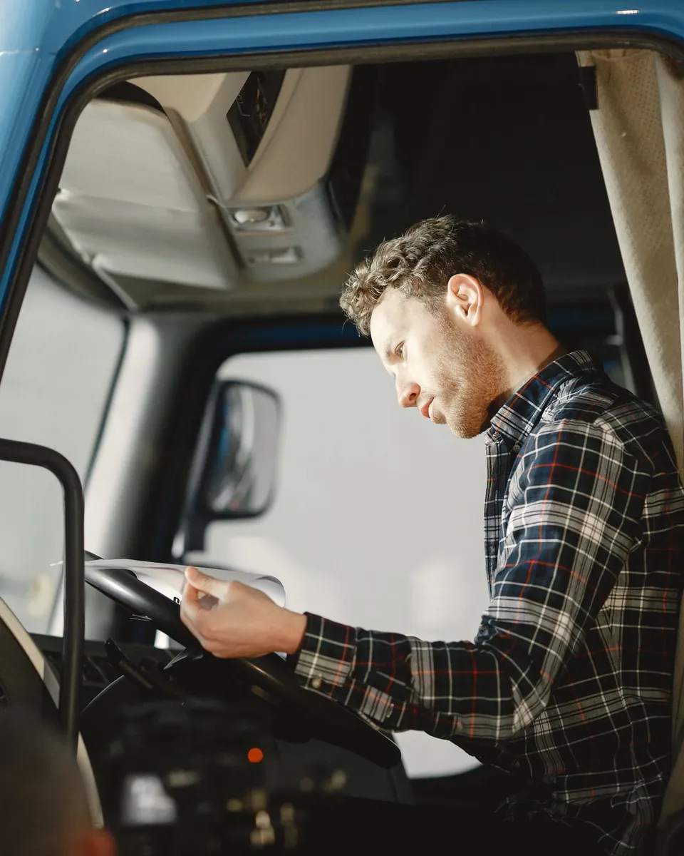 Truck driver in a plaid shirt reviewing paperwork in his cab