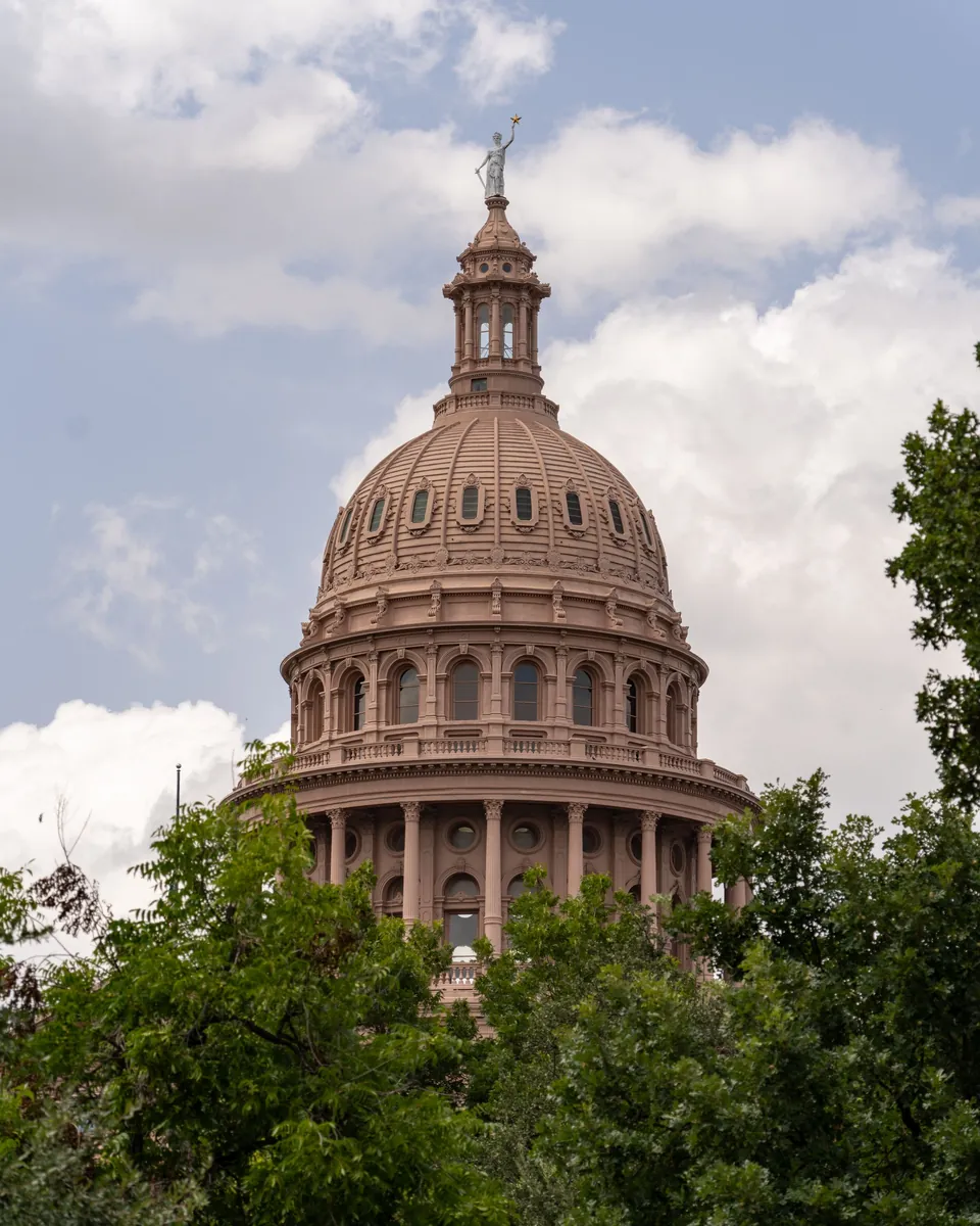 Texas State Capitol dome rising above green trees in Austin, TX