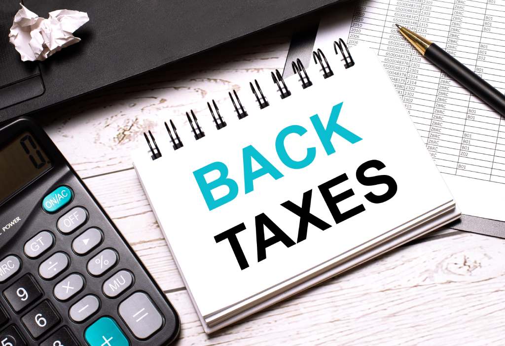 Back taxes in bold upper case blue and black font on notepad on desk