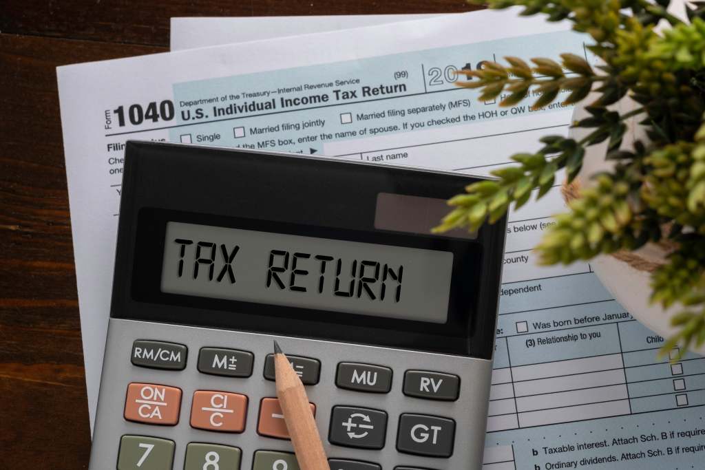 Tax returns words on calculator screen with 1040 tax return form in background 