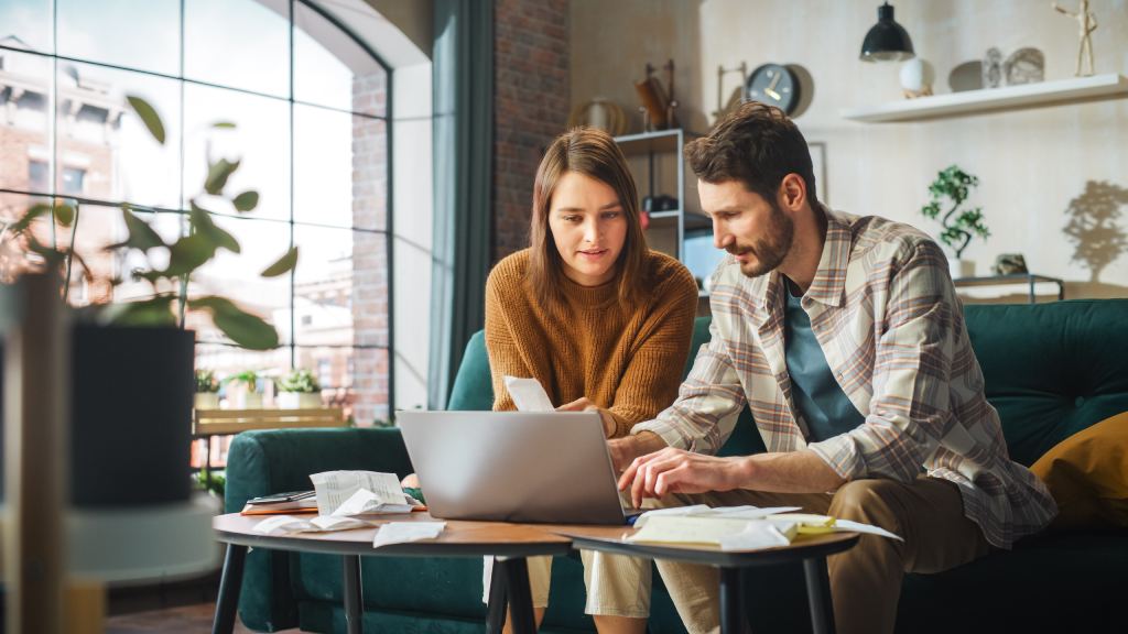 Young couple dealing with deferred tax liabilities using laptop on coffee table