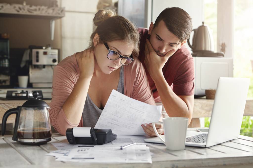 Young couple studying bills and trying to pay debt using laptop 