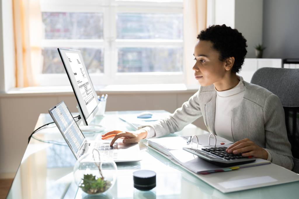 Young woman at desk using laptop and calculator to file tax returns in two states 