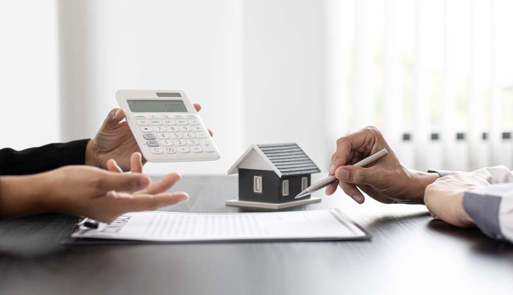 Close up of small model home and calculator on desk between people negotiating tax debt