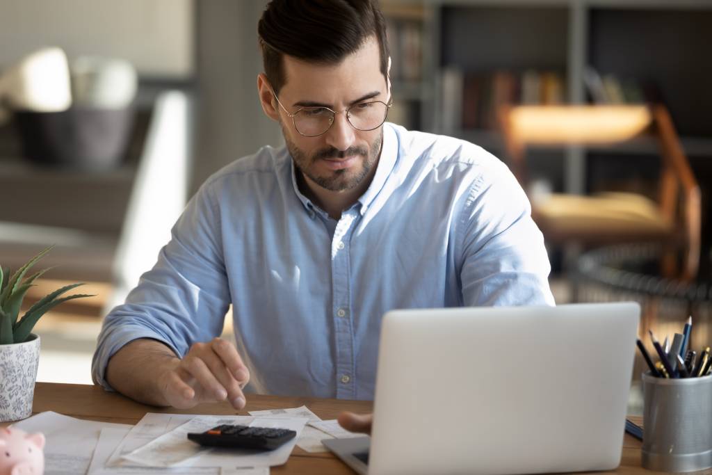 Man focused on laptop and typing on calculator to complete IRS tax return