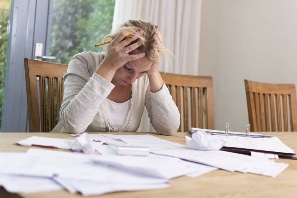 Woman sitting at desk with head in hands surrounded by unpaid tax bills 