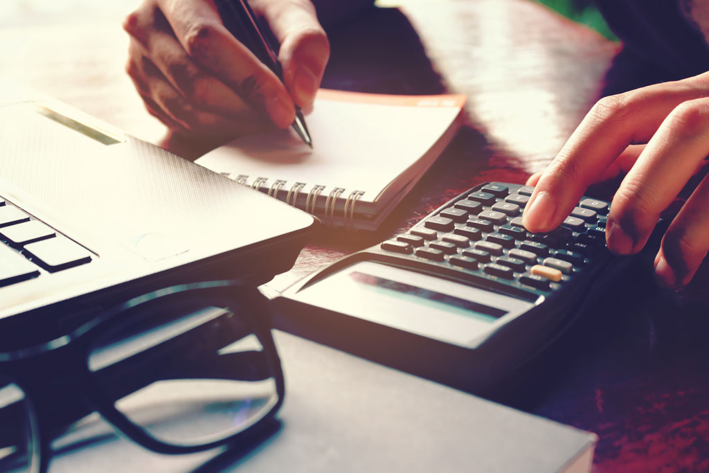  Close up of person calculating tax return with calculator and laptop open on desk